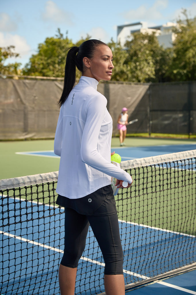 Women playing tennis wearing white relaxed mock zip top with black capri skorts. (Style 3002) - BloqUV