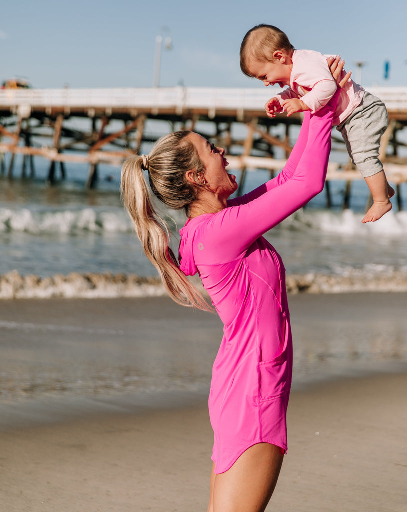 Women at the beach with her baby wearing bubble gum hoodie dress. Baby is wearing toddlers BloqUV in tickle me pink.(Style 2009) - BloqUV