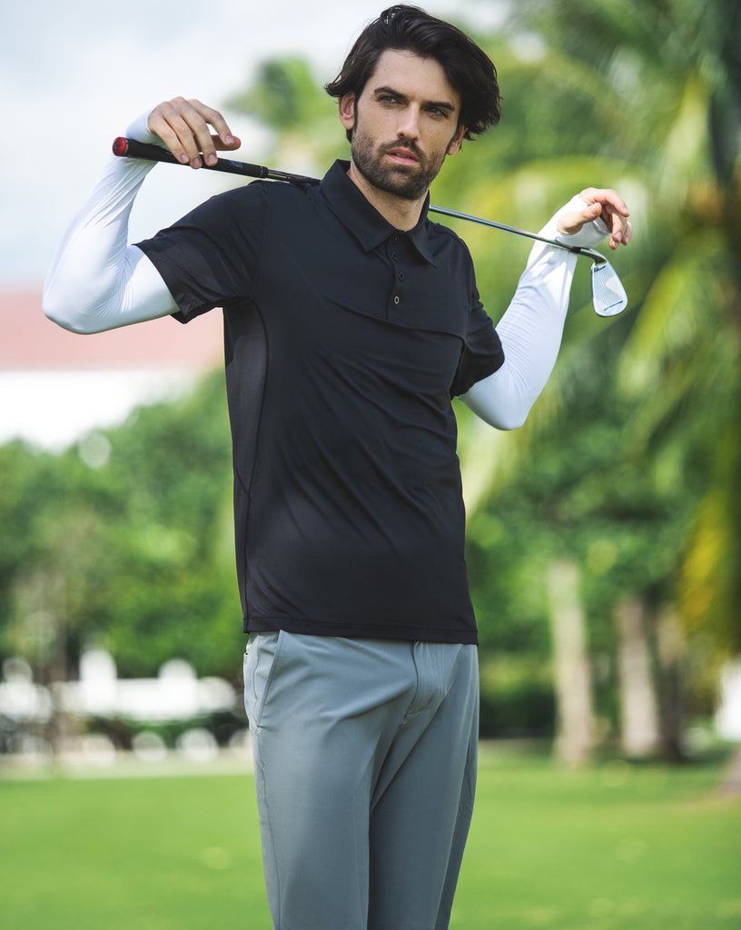Man outside posing with a golf club wearing a black polo shirt and white arm sleeves