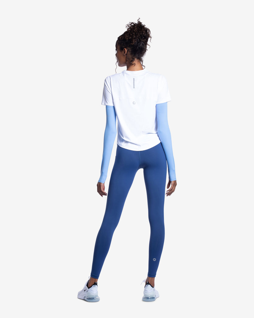 Women wearing white short sleeve crew top with indigo sun sleeves and navy tights. Picture shows the back of shirt showing reflector.(Style 1101) - BloqUV