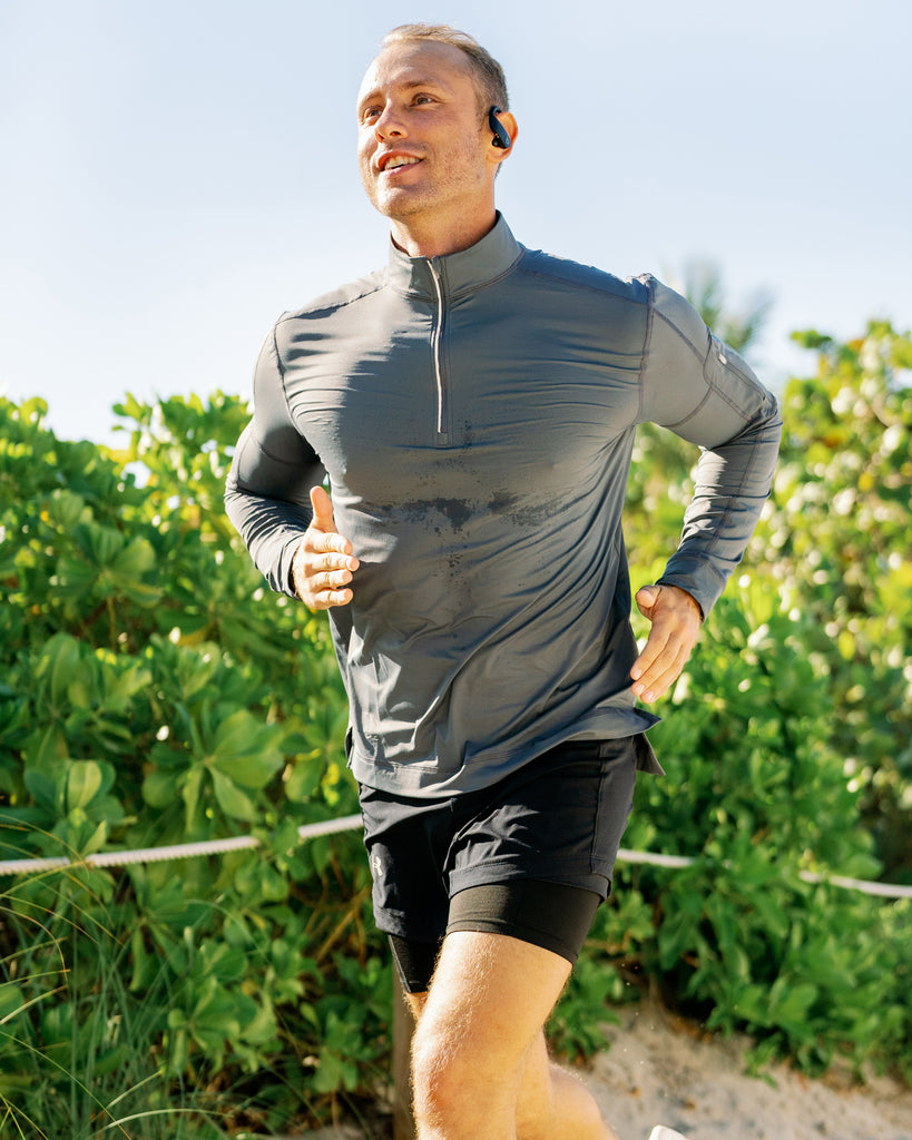 A man wearing a mock zip top with UPF 50+ long sleeves shirt running on a path near bushes.
