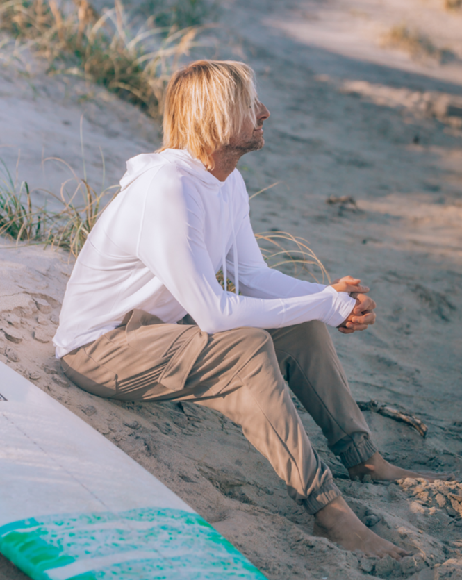 Man sitting on the sand wearing white unisex long sleeve hoodie shirt. (Style 12007) - BloqUV