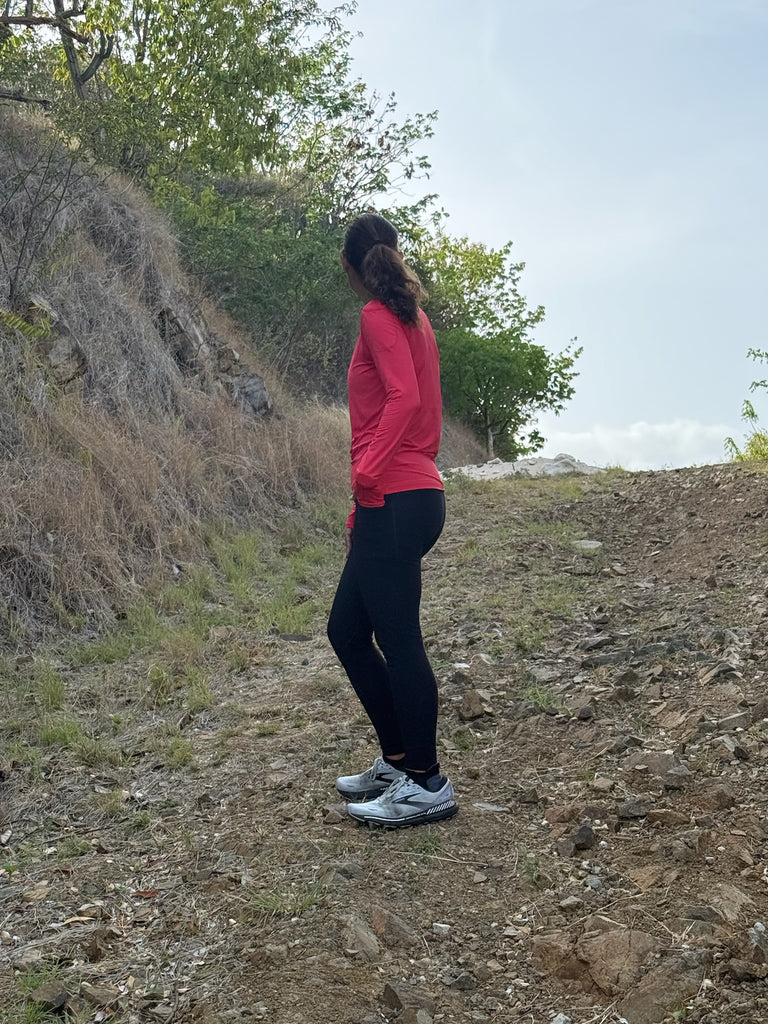 Person in red shirt and black pants standing on a rocky trail with trees in the background