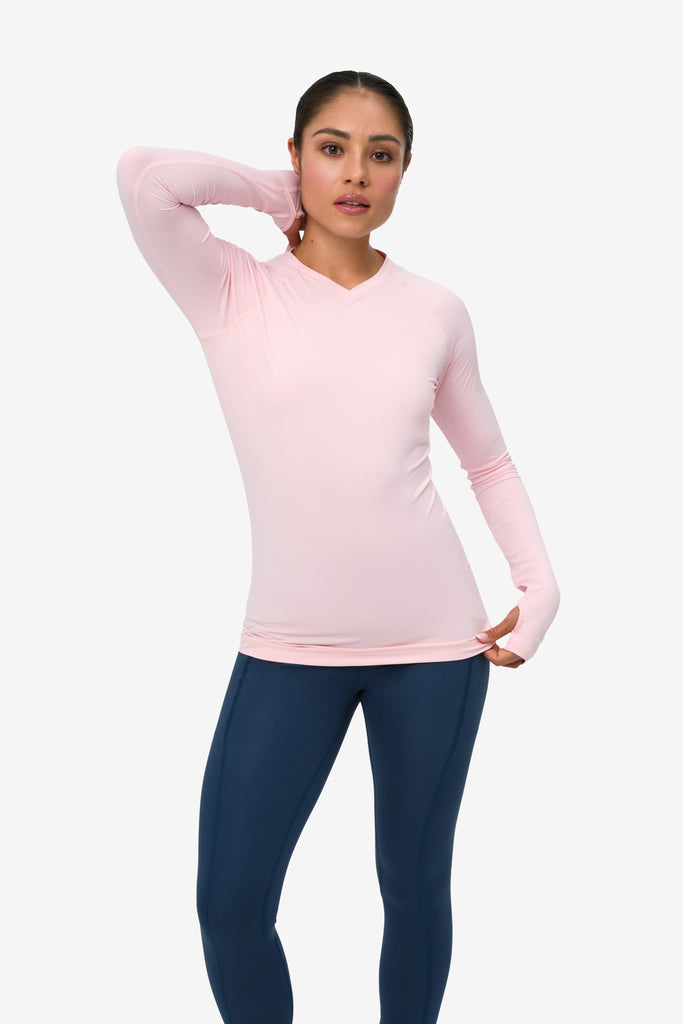 Woman wearing a pink long-sleeve top and navy leggings on a white background
