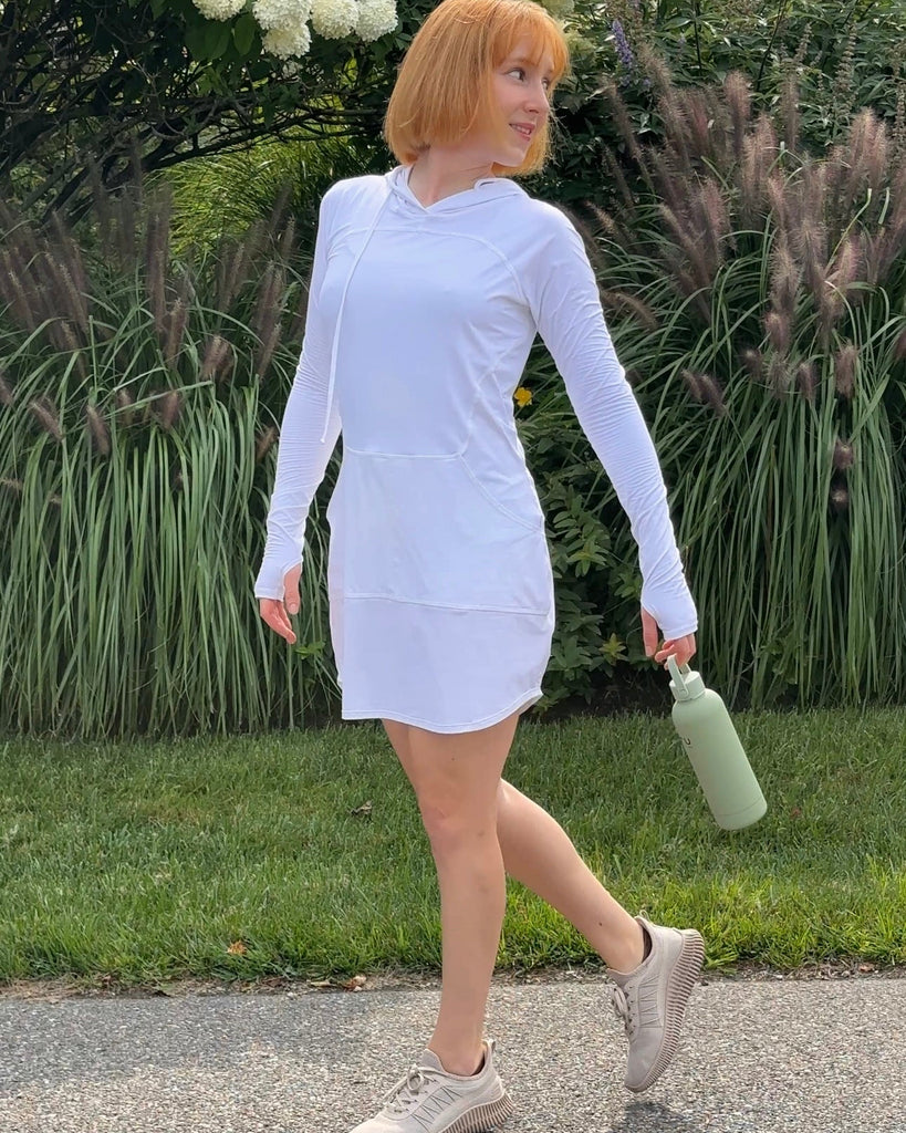Person wearing a white dress walking outdoors with greenery in the background