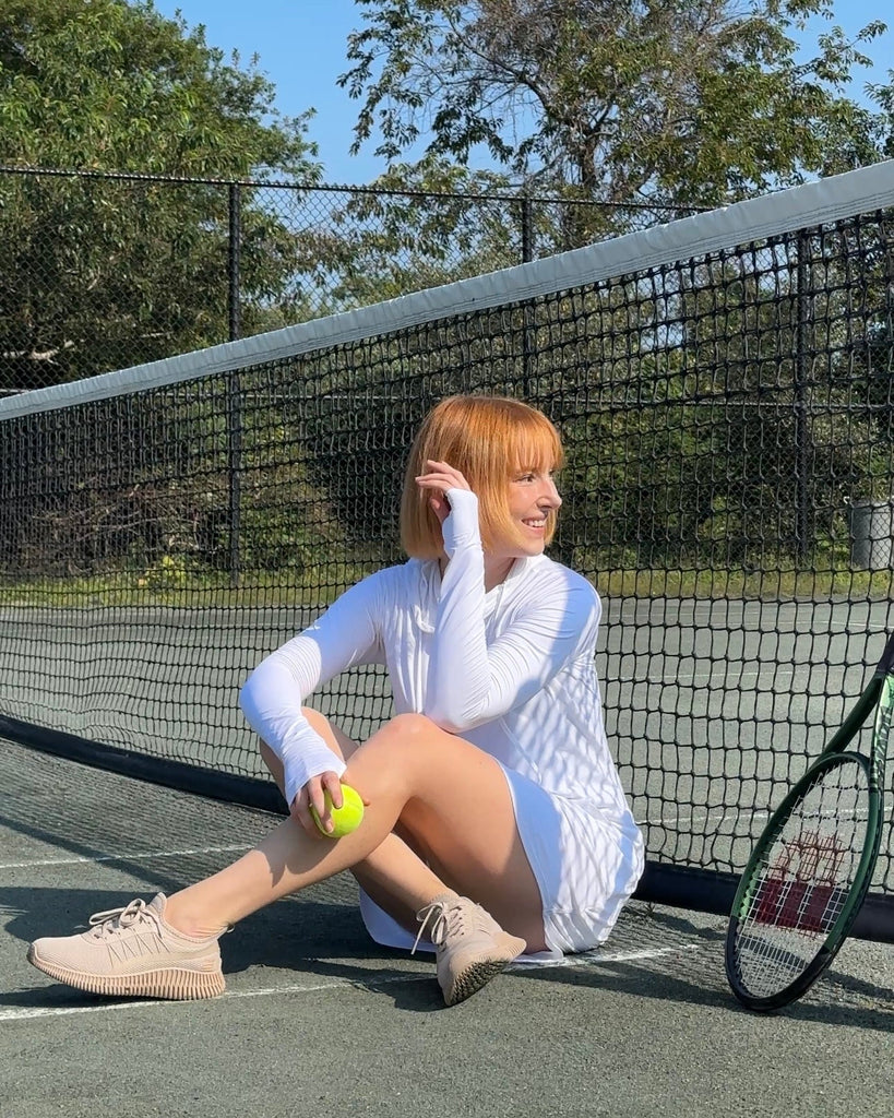 Woman sitting on a tennis court holding a tennis ball with a racket next to her.