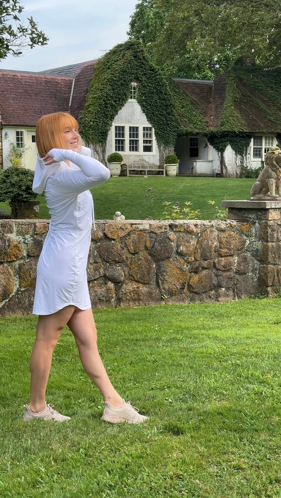 Person in a white dress standing in a garden with a stone wall and house in the background