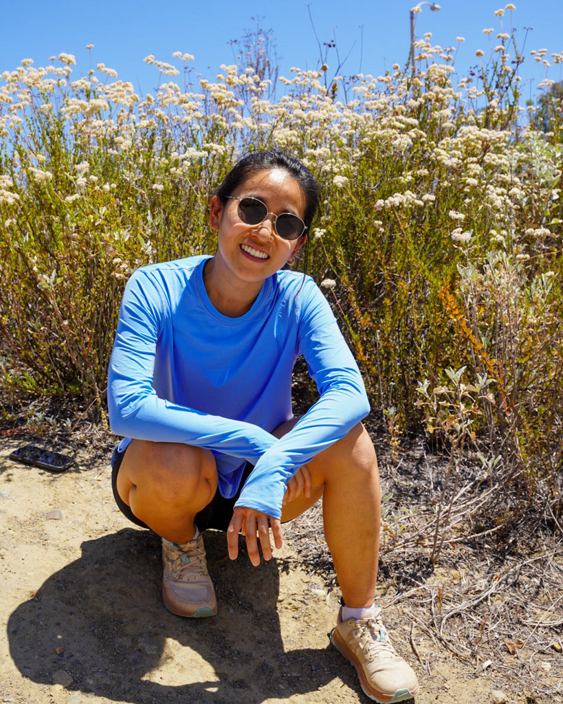 Person in a blue shirt and sunglasses crouching in a field of wildflowers