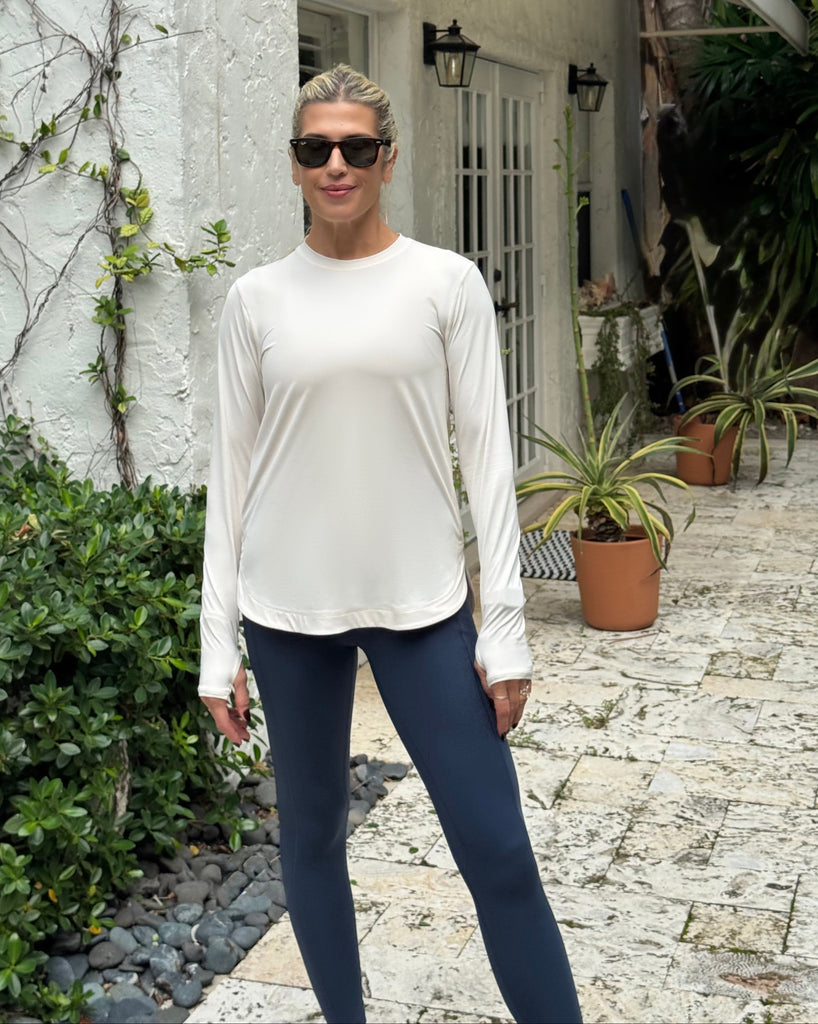 Person wearing a white long-sleeve shirt and blue leggings standing in front of a house with plants.
