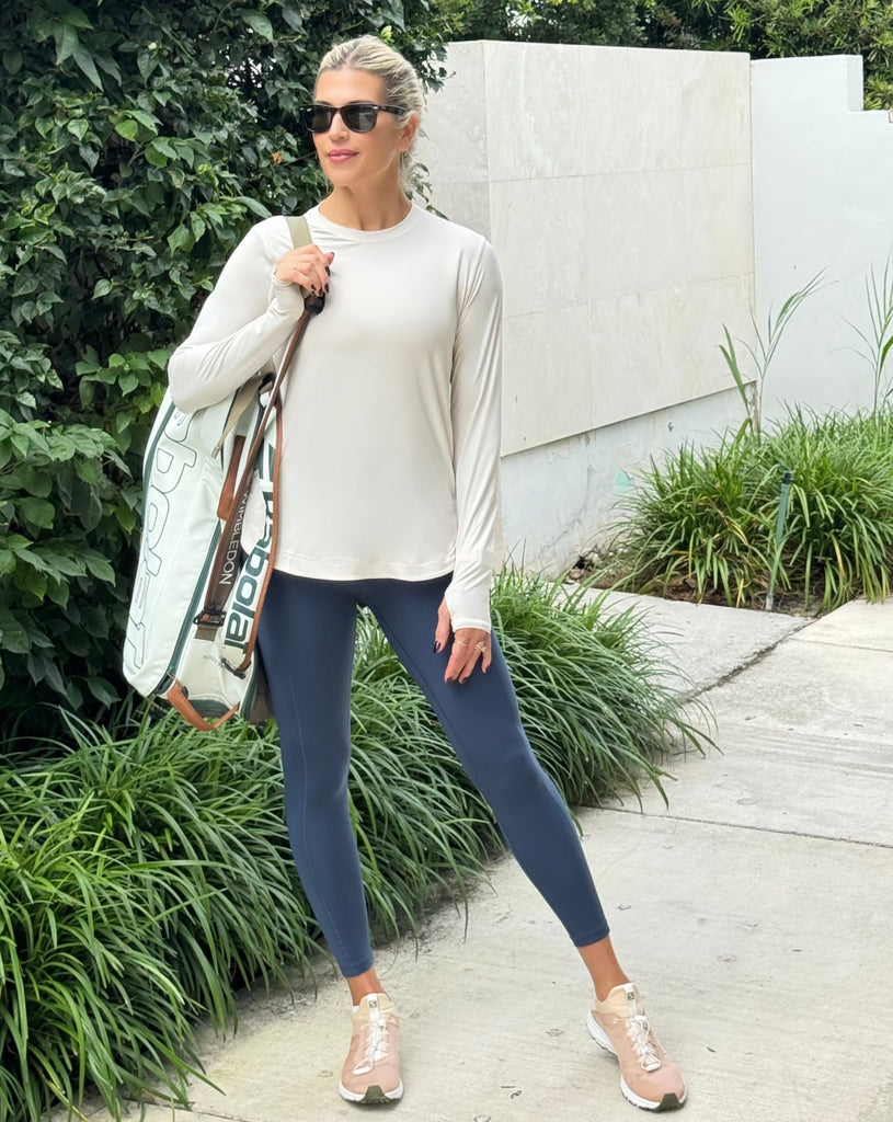Woman walking outdoors wearing a light-colored sweater, blue leggings, and sunglasses.