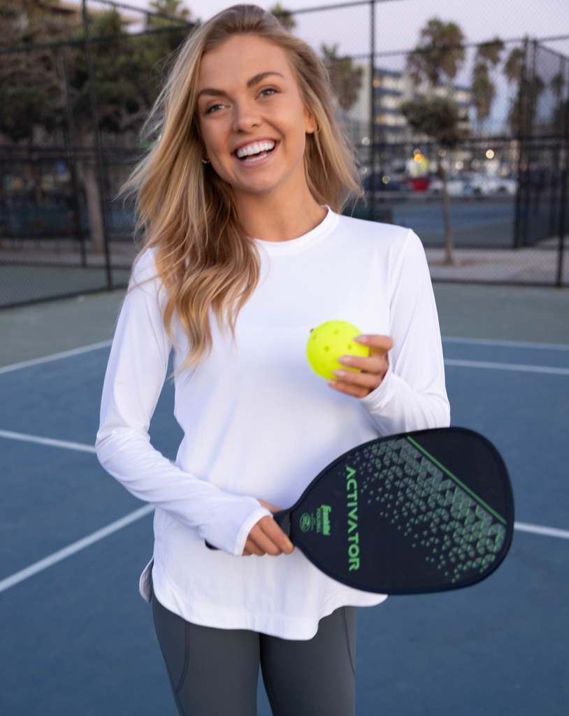 Women in tennis court  holding pickle ball racquet  wearing white long sleeve drawstring crew with smoke tights. (Style 2015) - BloqUV