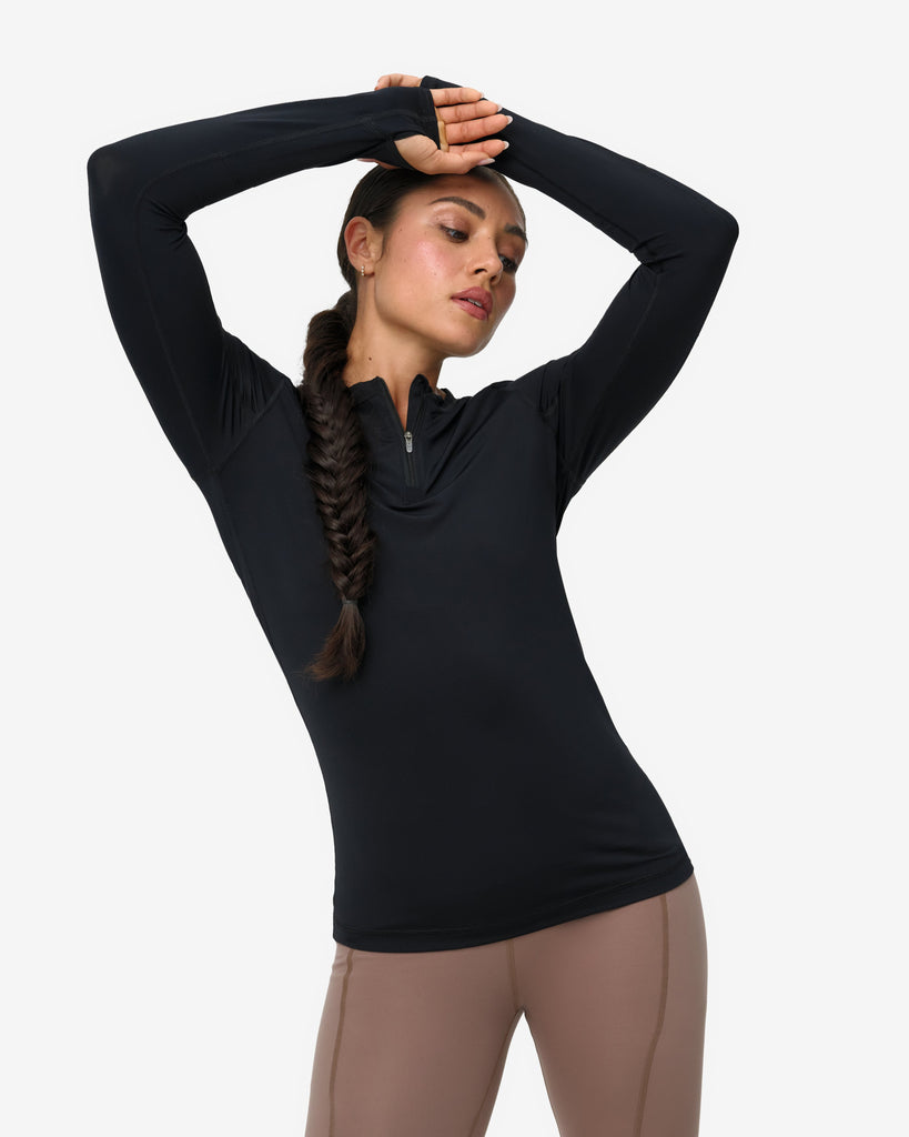 Woman wearing a black long-sleeve top and beige leggings on a white background