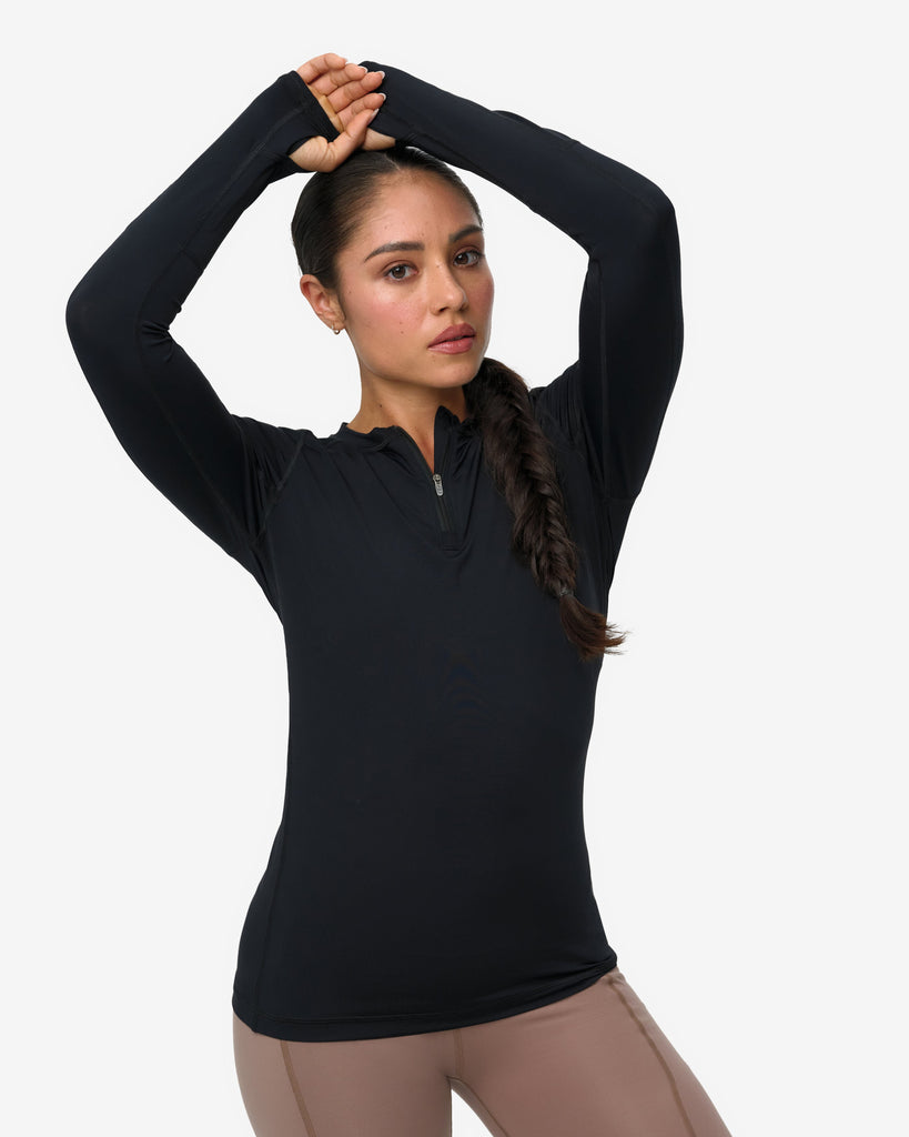 Woman wearing a black long-sleeve top and beige leggings on a white background