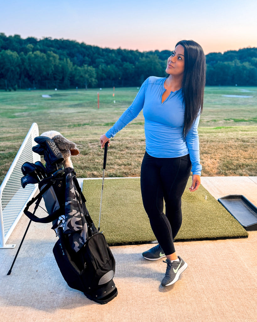 Woman standing on a golf course with a golf bag and club