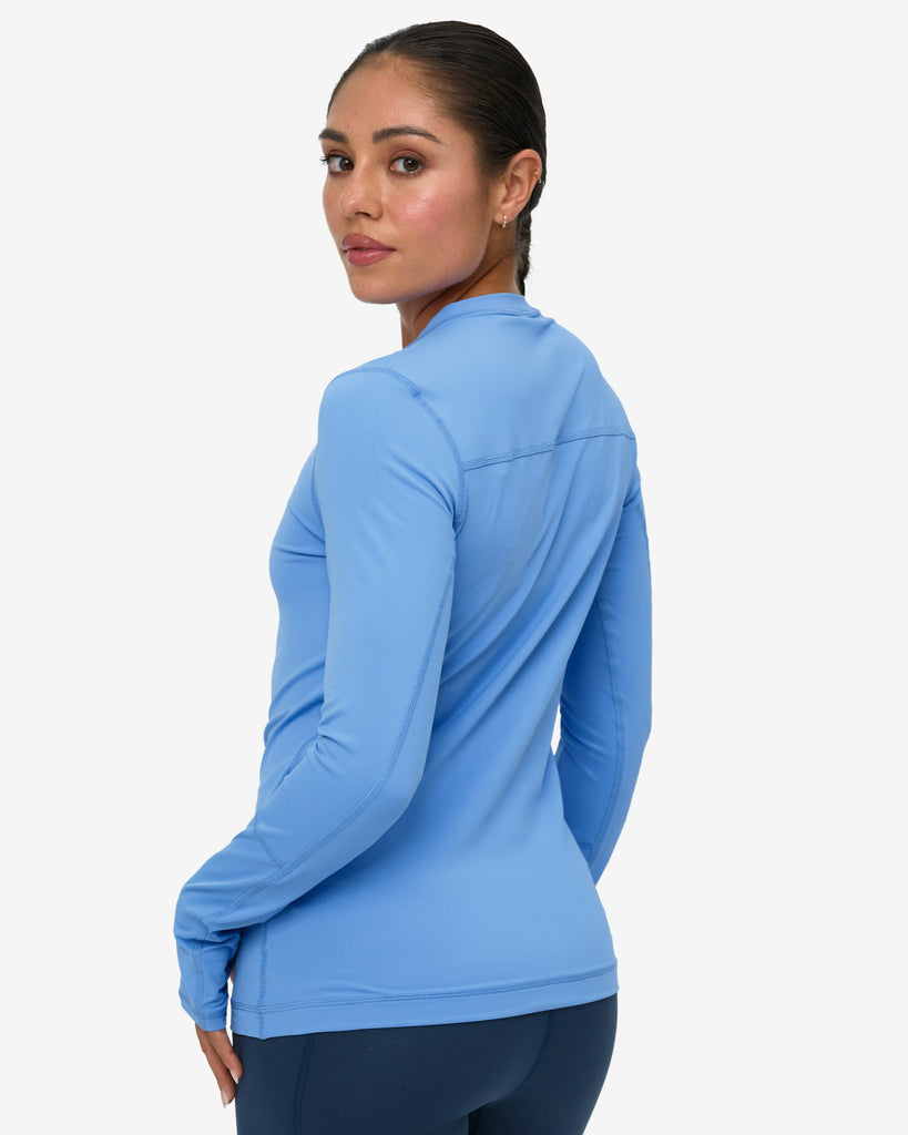 Woman wearing a blue long-sleeve top and dark blue leggings on a white background