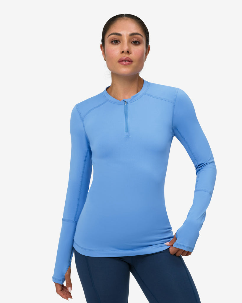 Woman wearing a blue long-sleeve top and dark blue leggings on a white background
