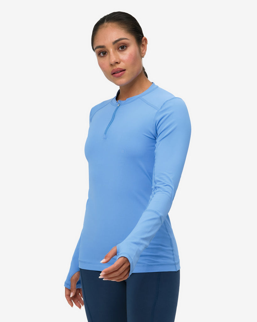 Woman wearing a blue long-sleeve top and dark blue leggings on a white background