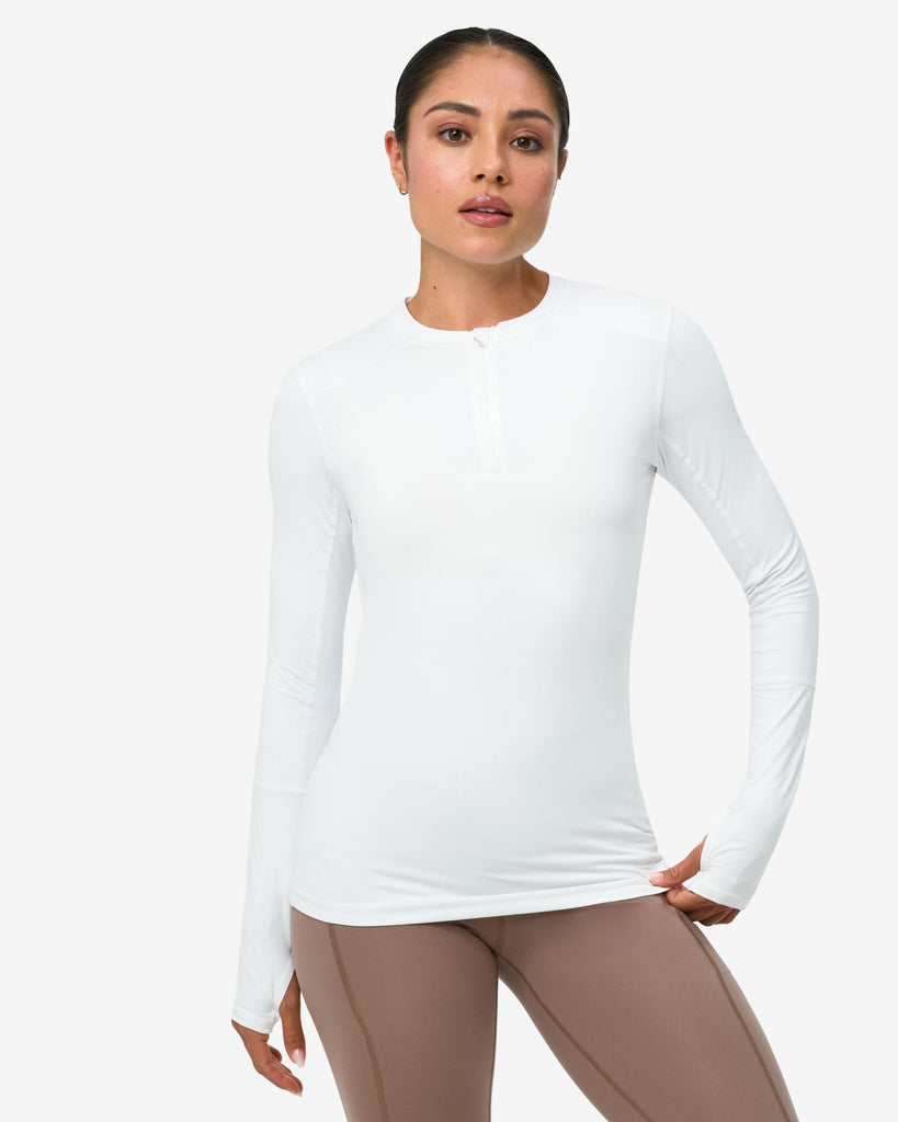 Woman wearing a white long-sleeve top and beige leggings on a white background