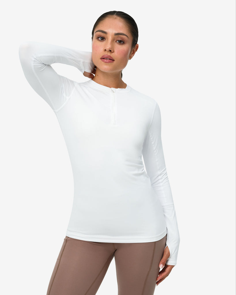 Woman wearing a white long-sleeve top and brown pants on a white background