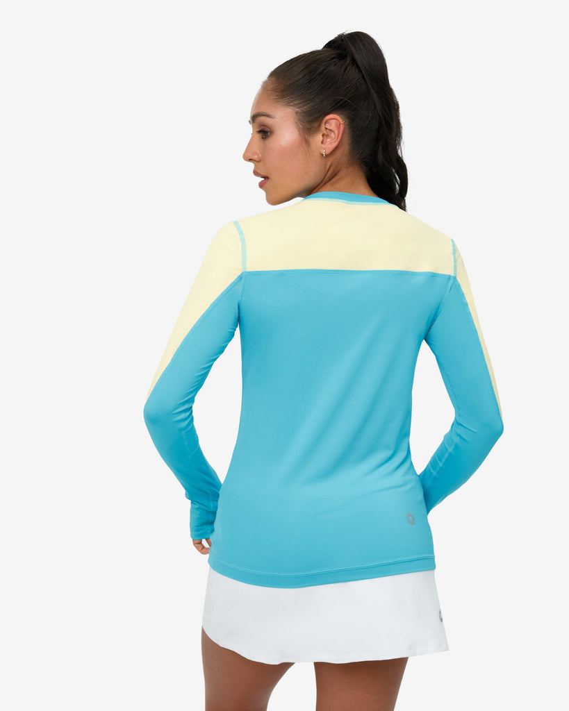 Woman wearing a blue and yellow long-sleeve top with a white skirt on a white background