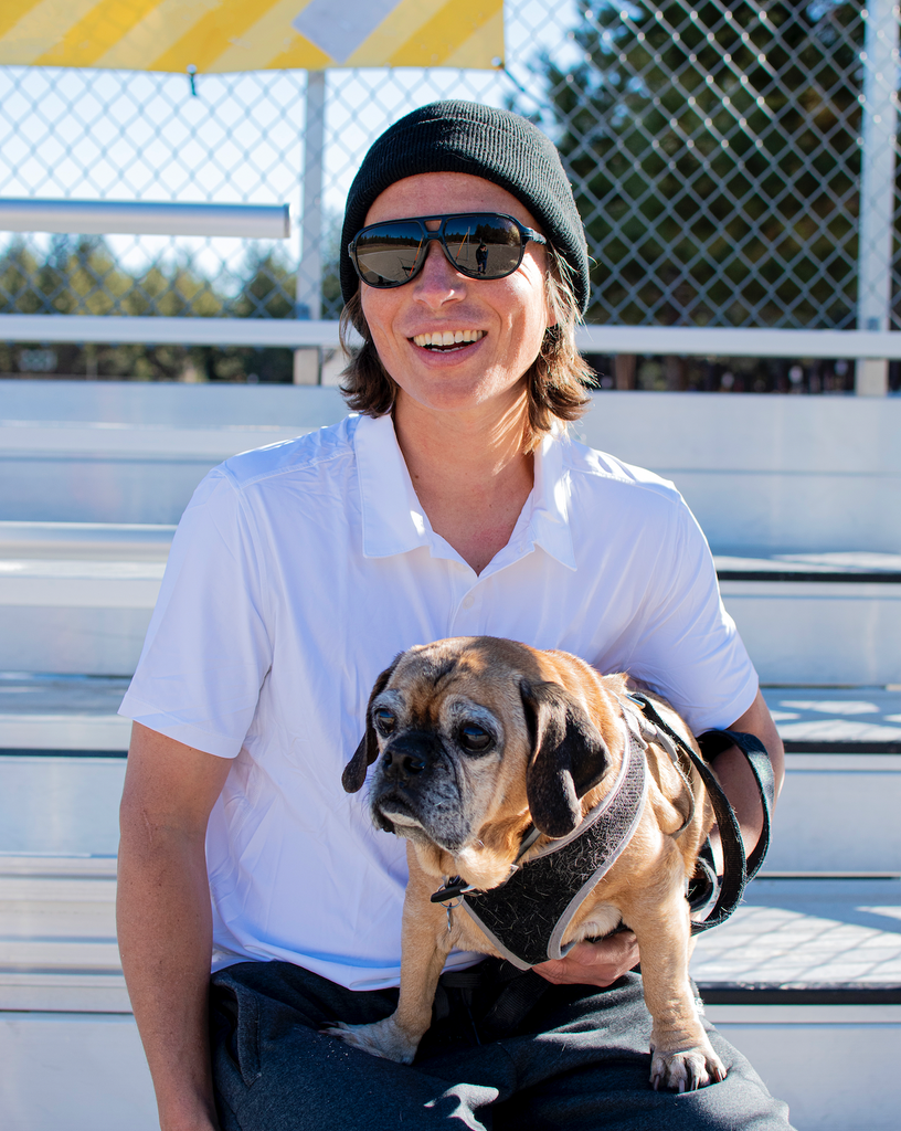 Man wearing white polo shirt sitting down smiling holding a dog 