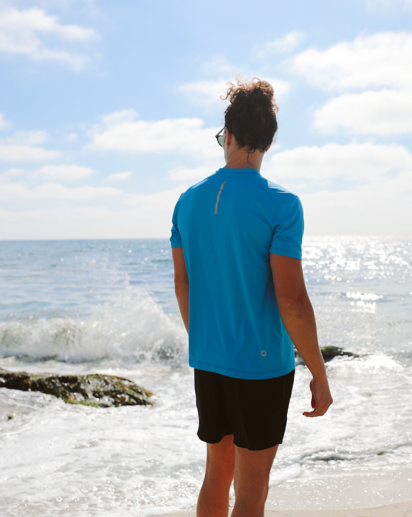 Man at the beach wearing short sleeve crew shirt in ocean Blue. Picture shows reflective trim in the back. (Style 11002) - BloqUV