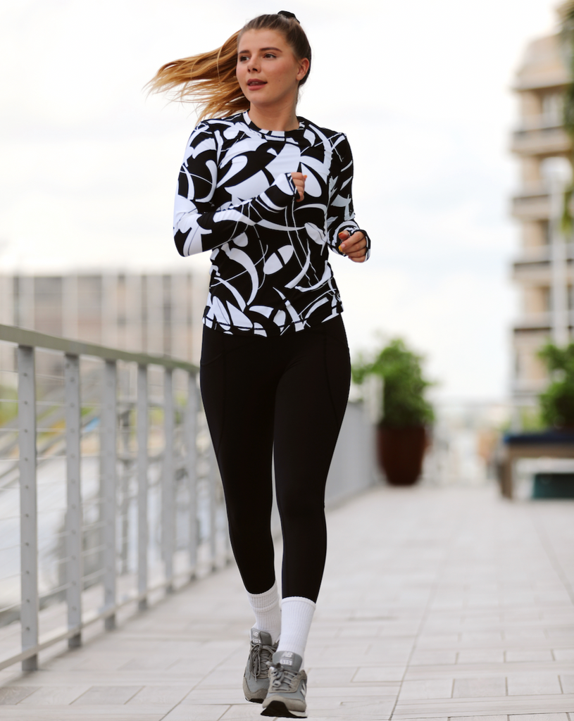 Women running outside wearing printed black and white long sleeve 24/7 shirt with black tights. (Style 2001J) - BloqUV