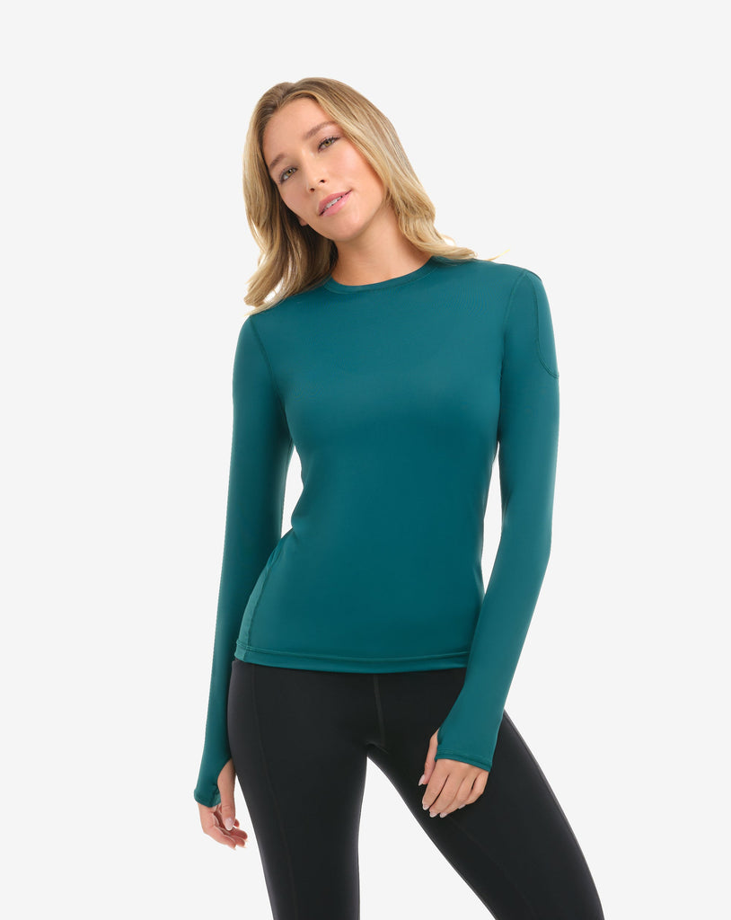 Woman wearing a teal long-sleeve top and black leggings on a white background