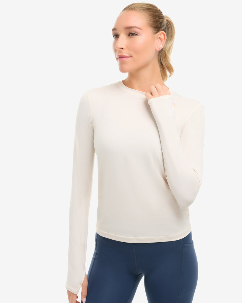 Woman wearing a cream sweater and navy leggings on a white background