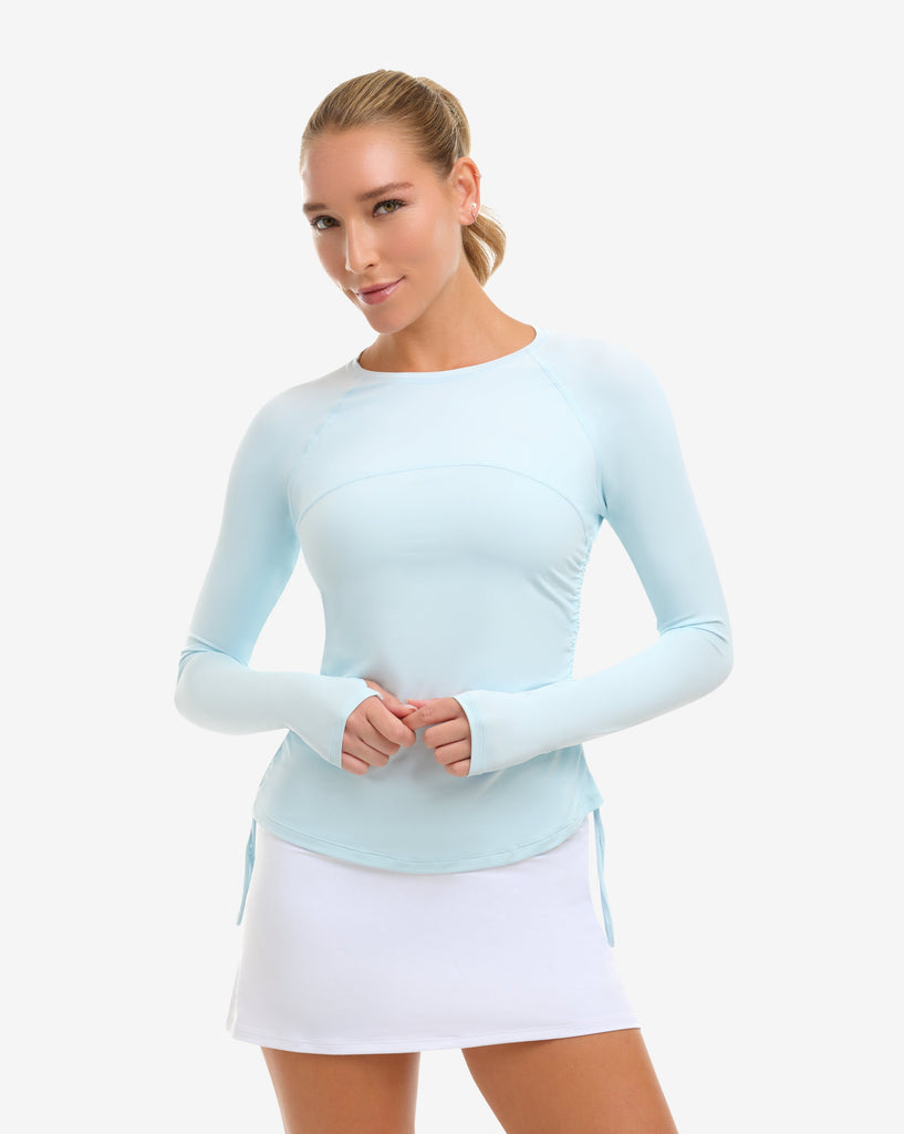 Woman wearing a light blue long-sleeve top and white skirt on a white background