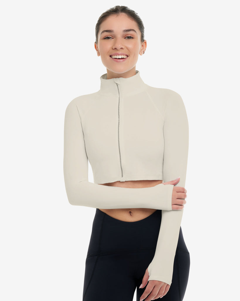 Woman wearing a beige long-sleeve top and black leggings on a white background