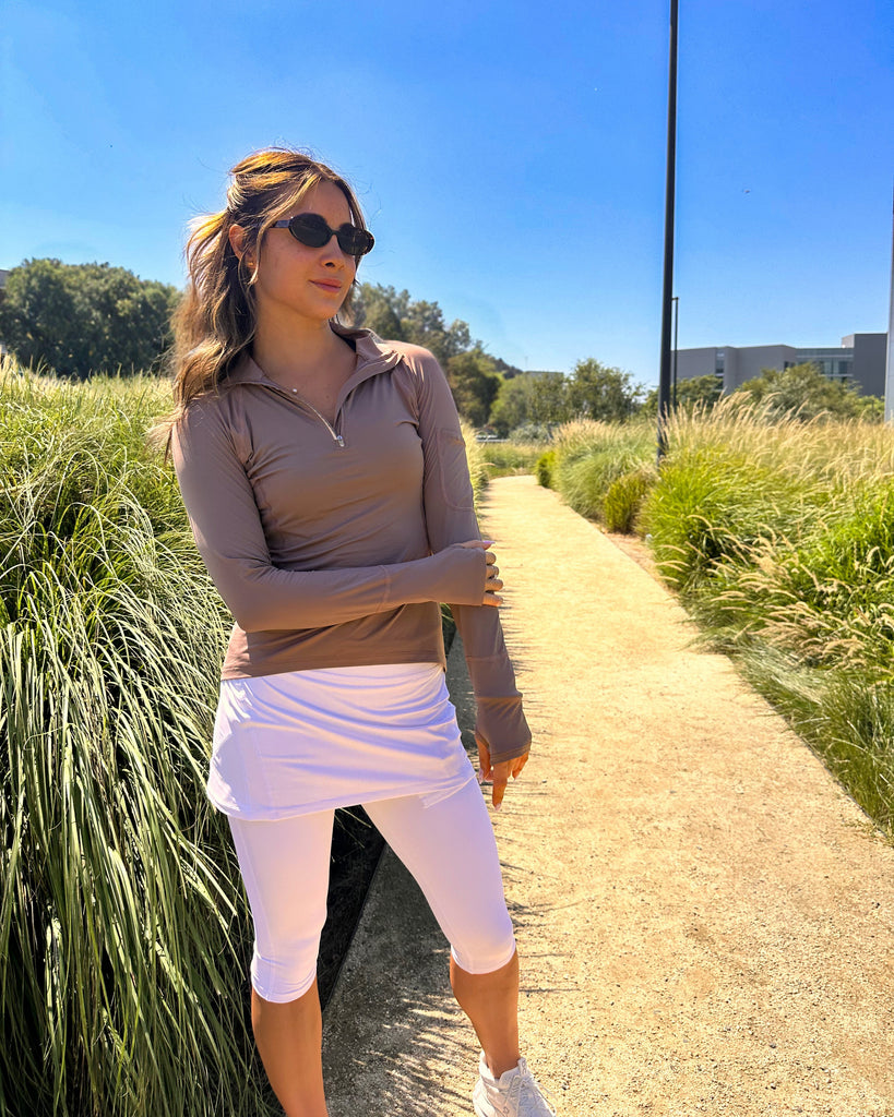 Woman in athletic wear standing on a path with greenery and a clear blue sky.