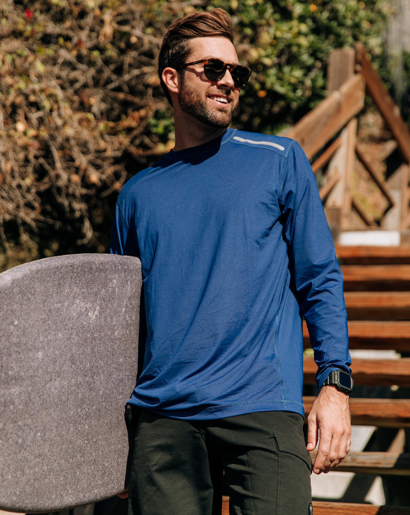 Man at the beach holding a surfboard wearing long sleeve jet tee shirt in navy blue. (Style 12002) - BloqUV