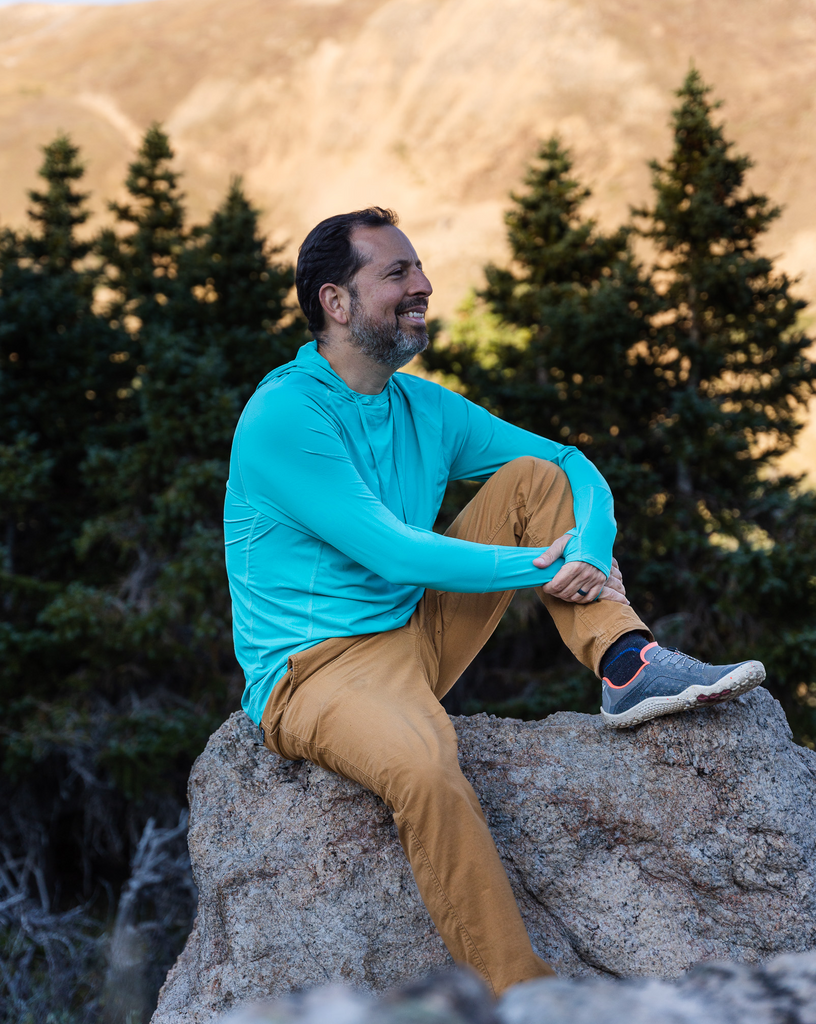 Man sitting on rock wearing caribbean blue color unisex long sleeve hoodie shirt. (Style 12007) - BloqUV