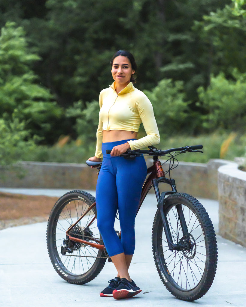 Women standing by her bicycle wearing lemon yellow full zip crop top with navy leggings. (Style 4010) - BloqUV