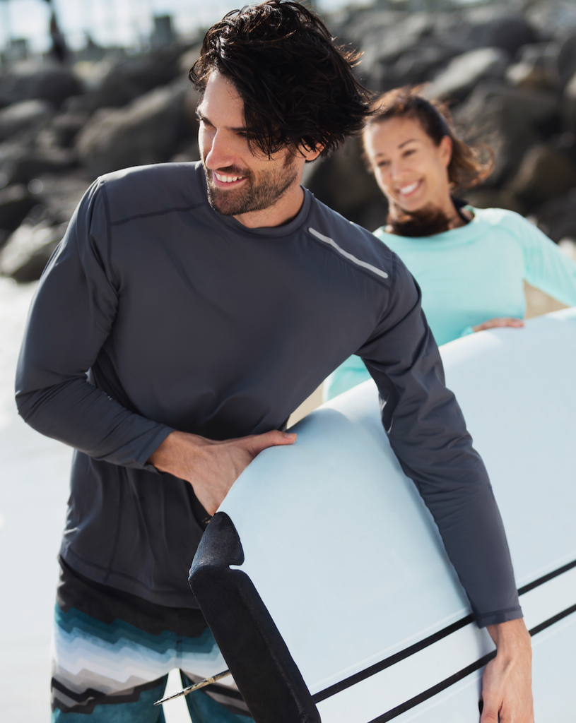 Man holding a surfboard at the beach wearing long sleeve jet tee shirt in smoke. (Style 12002) - BloqUV